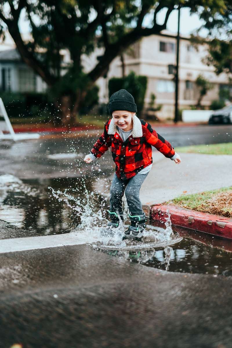 Rain boy in red and black jacket and black knit cap running on wet road during daytime
