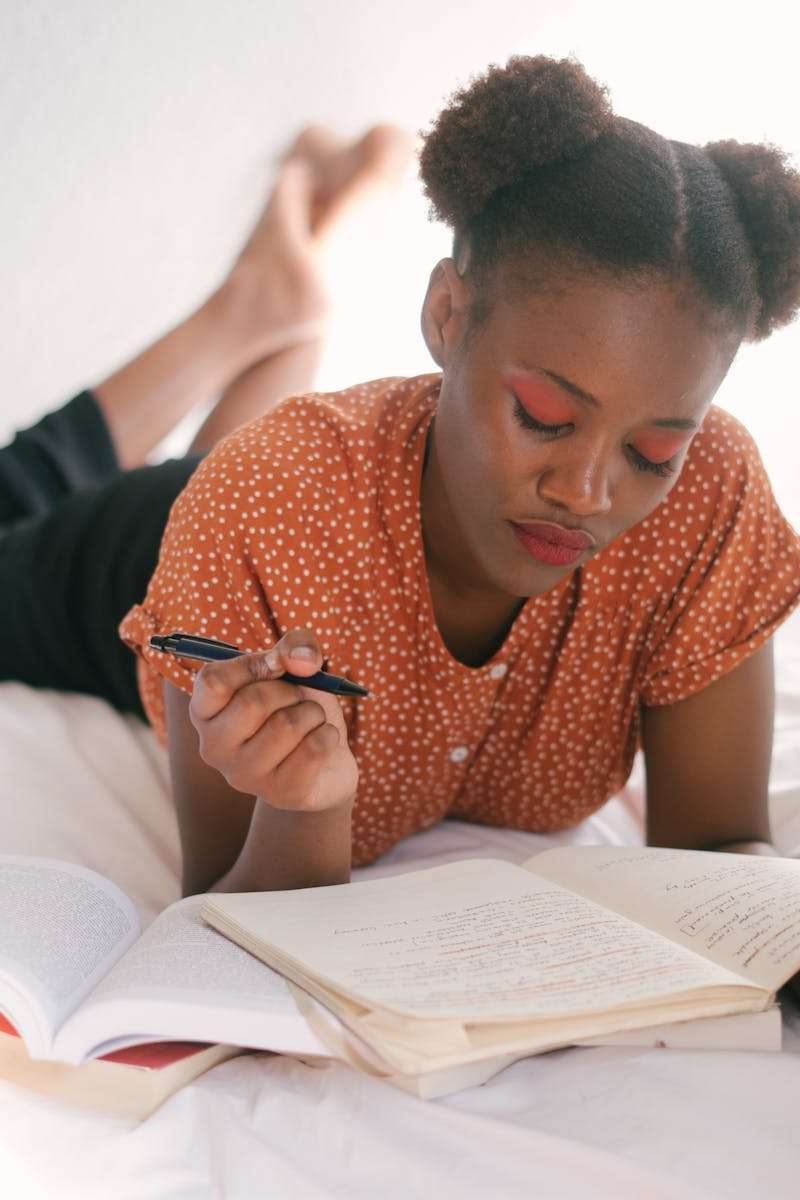 Autism in teens and adults A young black woman lying down while writing in a notebook, looking relaxed.