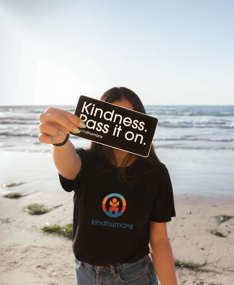 kindness alphabet a woman holding up a sign on the beach