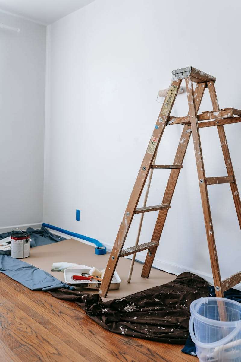 Remodeling projects A home renovation scene featuring a wooden ladder, painting tools, and white walls in a room.