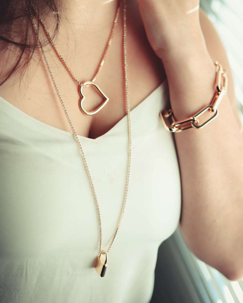 Jewelry gold pendants Close-up of woman wearing gold heart-shaped necklace and chunky bracelet.