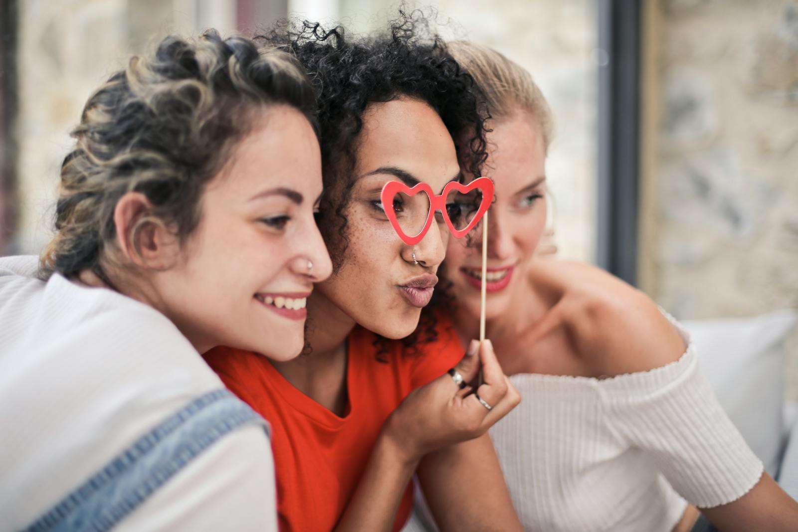 friends, family and family friends Three women enjoying a playful moment with heart-shaped glasses, symbolizing friendship and fun.