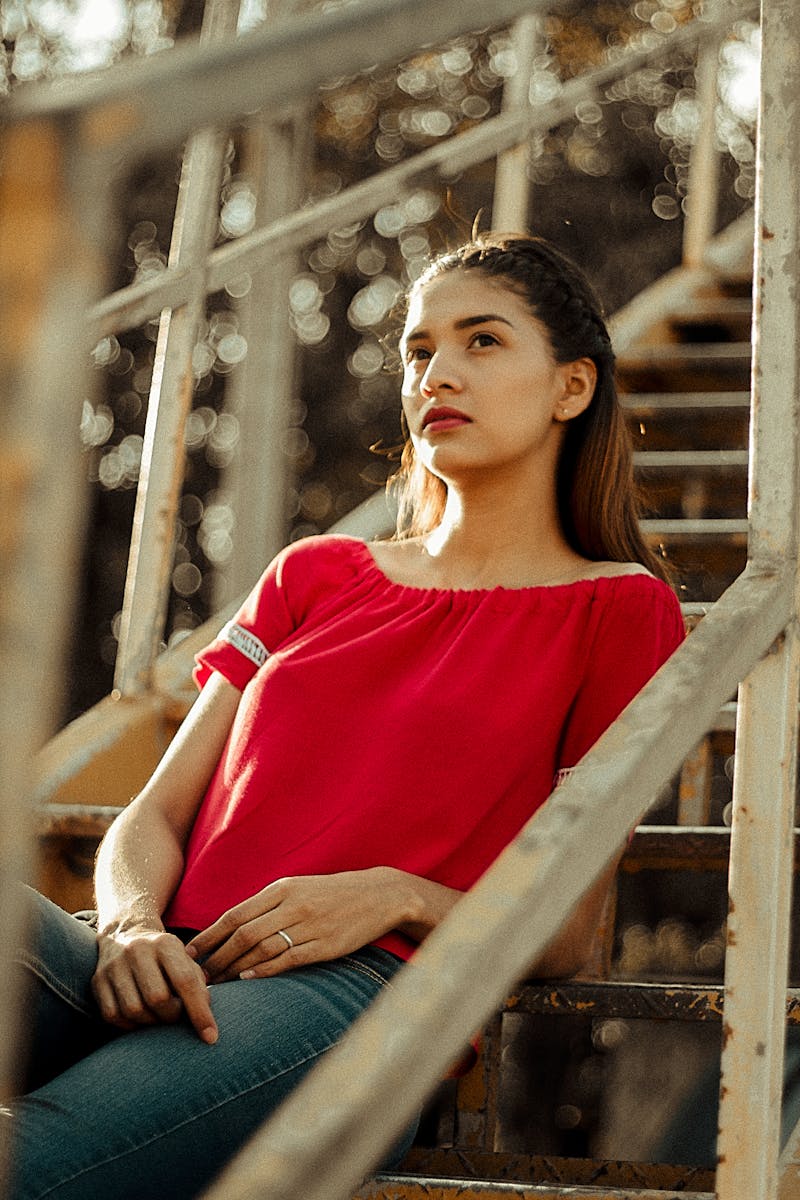 Emotional baggage A young woman in a red top sits thoughtfully on outdoor stairs, bathed in warm sunlight.