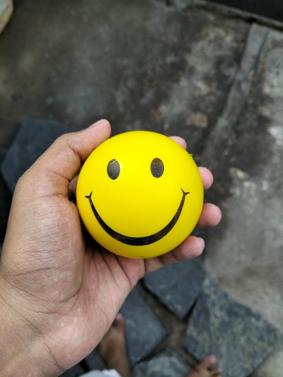 7 Lifestyle Habits That Enhance the Effectiveness of Skin Supplements A hand holds a yellow smiley face stress ball.