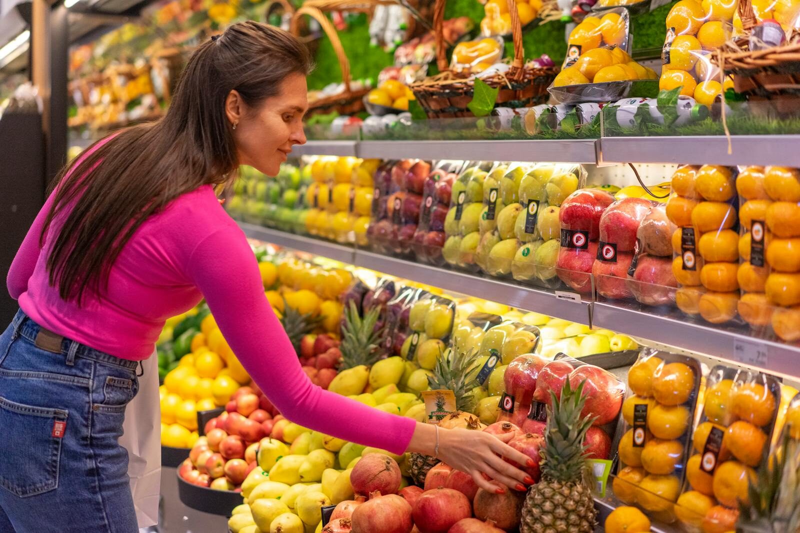 The Beginner's Guide to Reducing Synthetic Additives in Your Daily Diet A woman in a bright pink top selecting fresh fruits in a grocery store produce aisle.