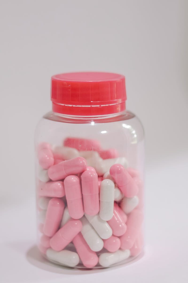 How to Read Supplement Labels to Ensure Quality and Safety Close-up of pink and white capsules in a transparent jar with pink lid for healthcare use.
