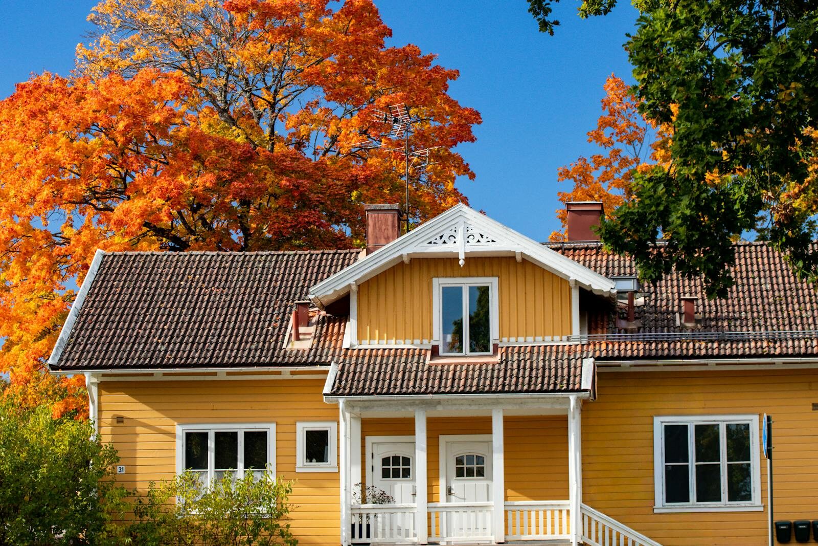 Proactive Roof Maintenance: Essential Tips to Extend Your Roof's Lifespan Yellow Scandinavian house surrounded by vibrant autumn leaves in Jönköping, Sweden, under a clear blue sky.