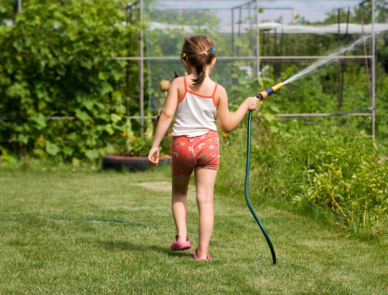 Water-Smart Irrigation Techniques for a Healthier Lawn Back view of a young girl watering a garden with a hose on a sunny day.