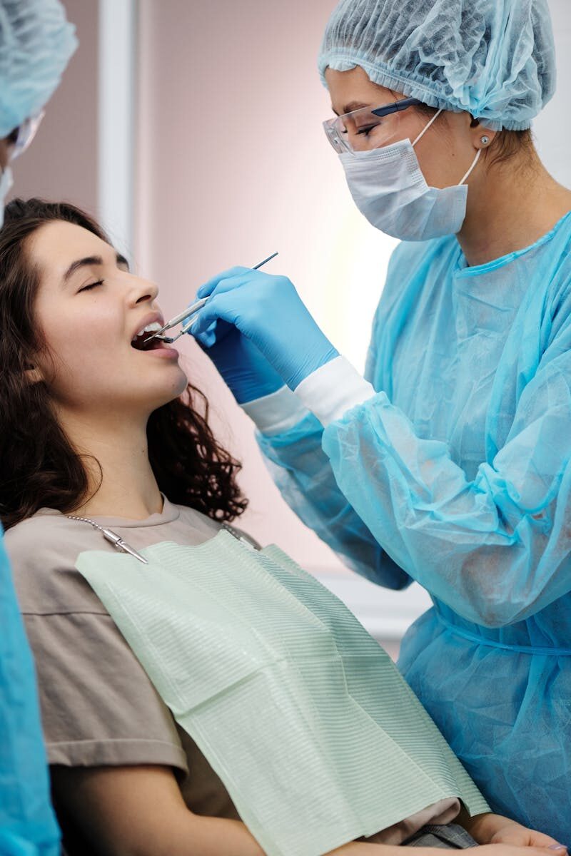 Dental Implants: A Comprehensive Guide to Modern Tooth Replacement Options Dentist in protective gear examining a woman's teeth during a dental clinic visit.