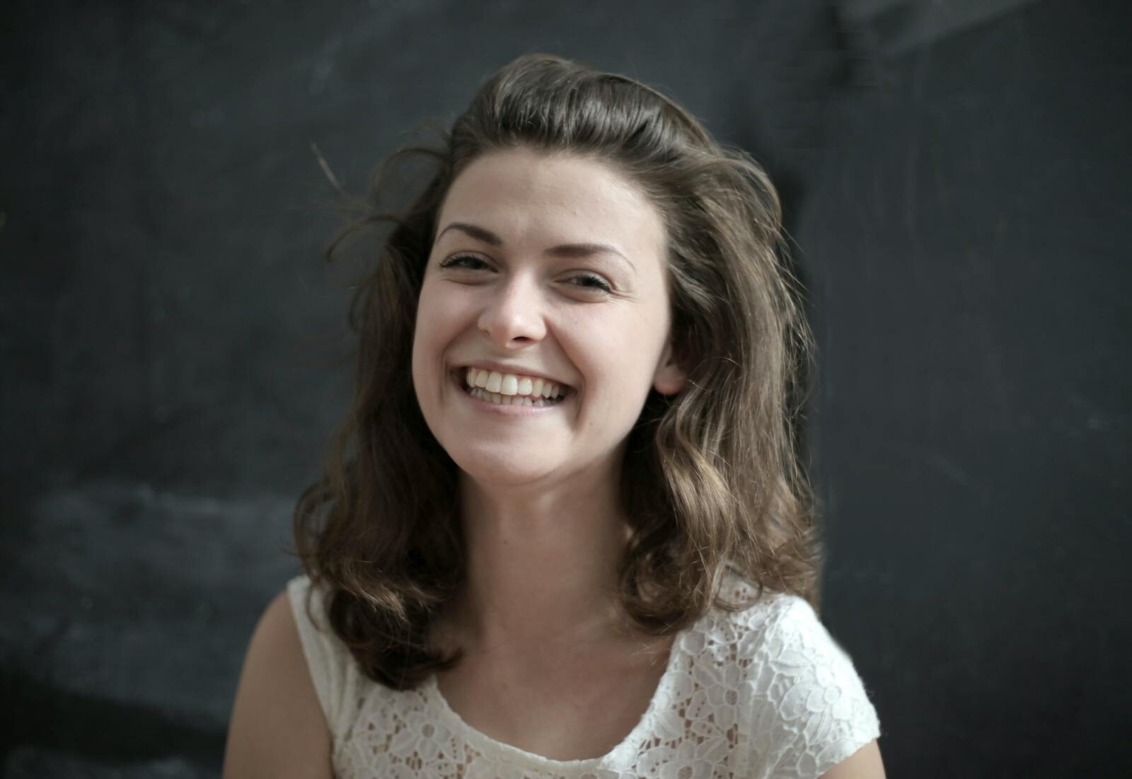 The Link Between Oral Health and Overall Health: What the Research Actually Shows Portrait of a cheerful woman with a radiant smile against a dark backdrop.