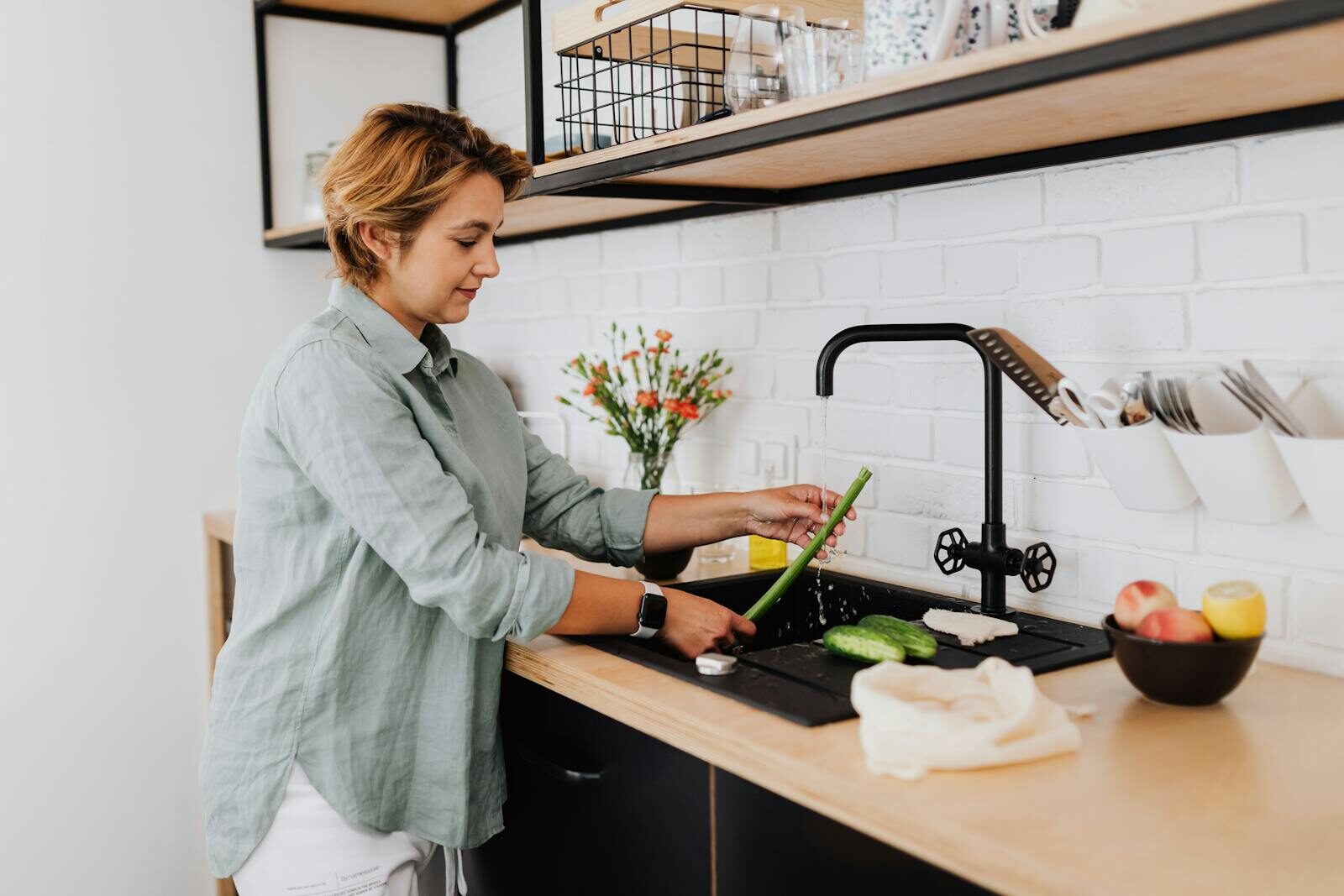 Why Low Water Pressure is More Than Just a Nuisance for Your Home A woman washing vegetables in a stylish kitchen with contemporary decor.