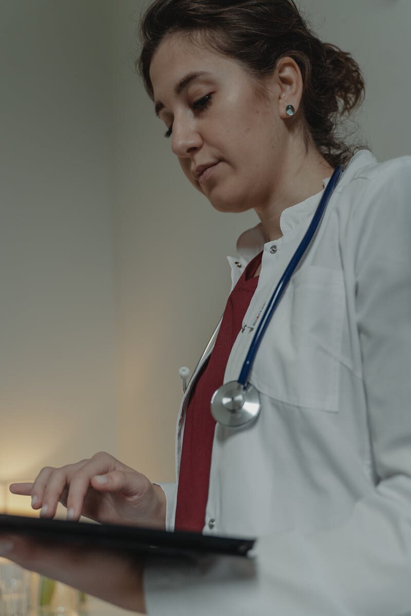 Comprehensive Guide to Intensive Outpatient Programs (IOPs) A professional female doctor uses a digital tablet in a well-lit clinic setting, wearing a stethoscope and lab coat.