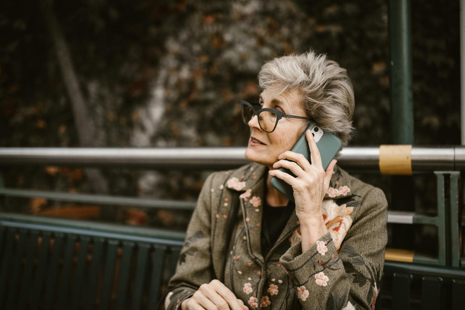 How Technology Is Revolutionizing Senior Safety and Independence Elderly woman with glasses talking on a smartphone while seated outdoors.