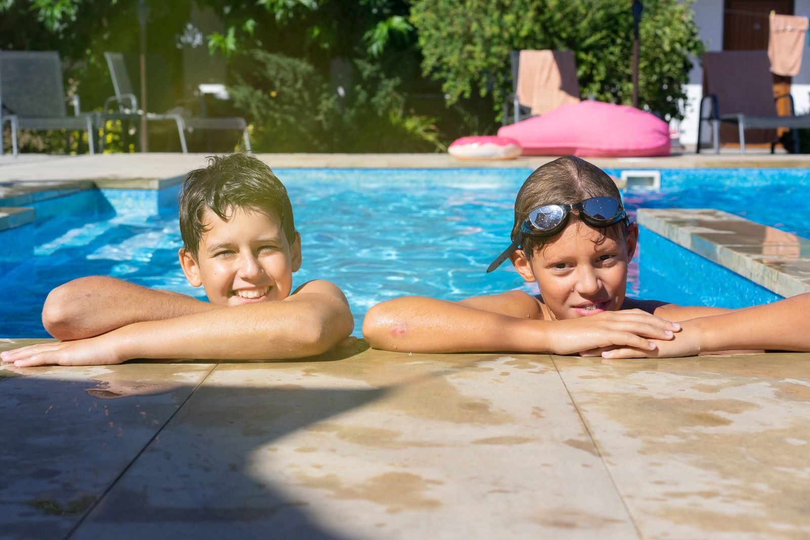 What to Know Before Hiring a Custom Pool Builder in Phoenix Two kids smiling and relaxing in a swimming pool, enjoying a sunny vacation day.
