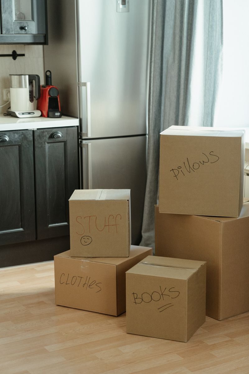 The Ultimate Moving Across the Country Checklist in 2026 Cardboard boxes labeled with contents in a kitchen, suggesting a recent move-in.