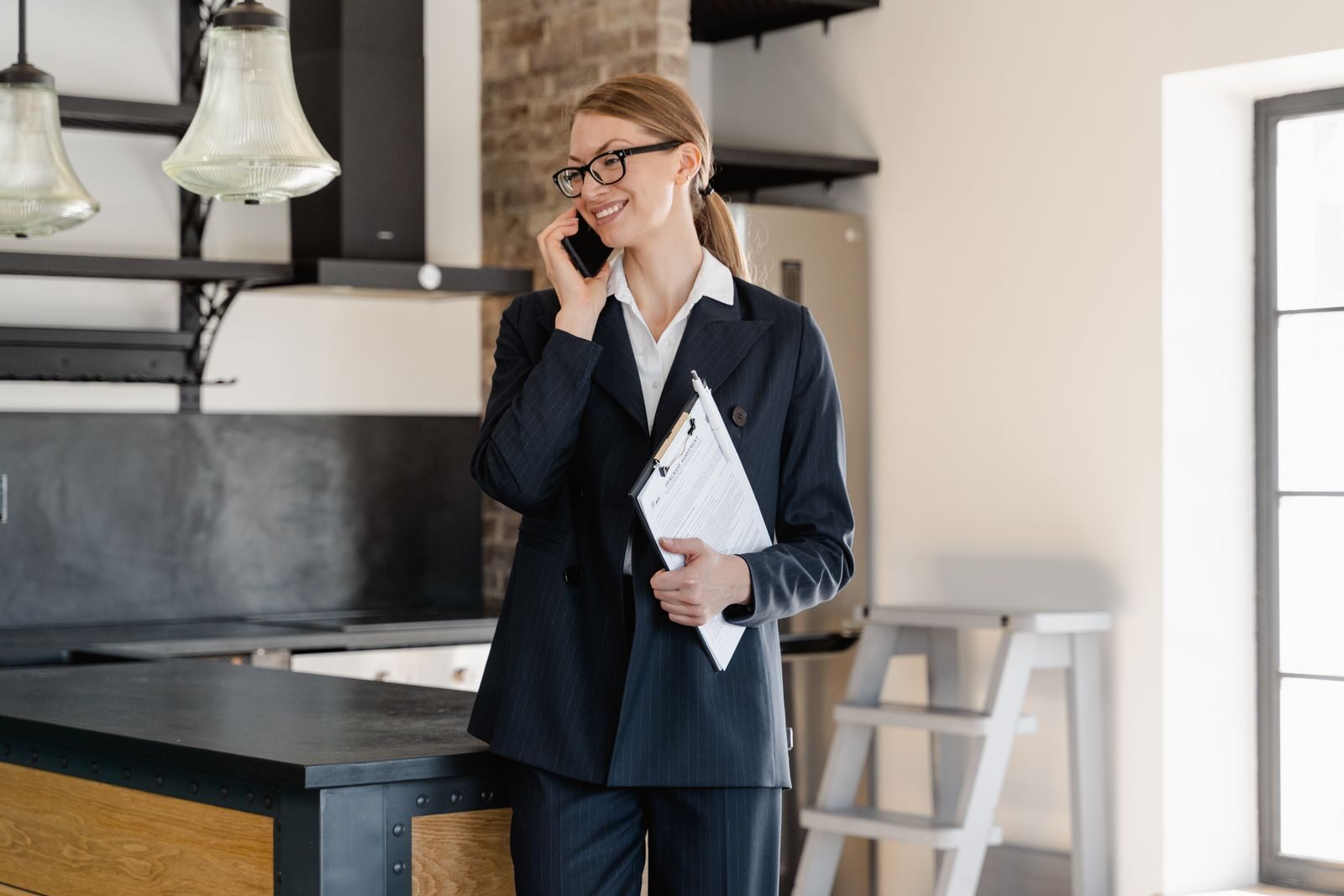 The Essential Role of a Transaction Coordinator in Real Estate Confident businesswoman in office attire making a call while holding a clipboard in a modern workspace.