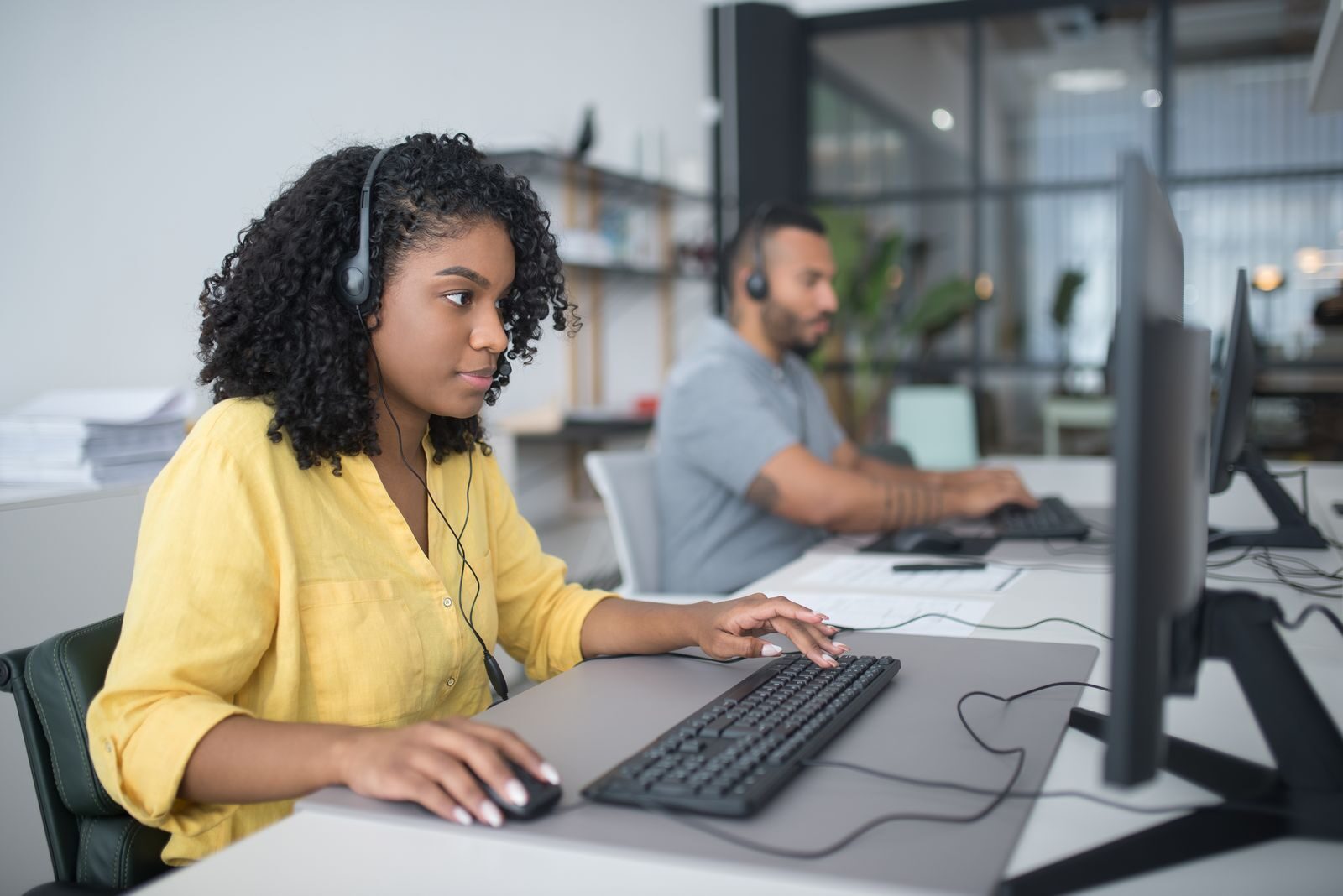 Norbert Vergez: Why Cybersecurity Is a Core Requirement in Modern Project Management Two customer service agents working with headsets in a modern office setting.