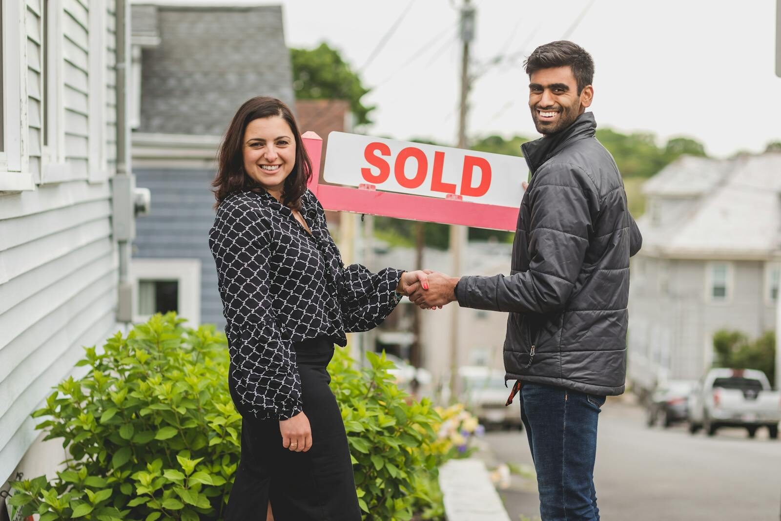 Selling Your House As-Is: A Step-by- Step Guide for HomeownersTwo people shake hands in front of a sold sign, celebrating a real estate deal.