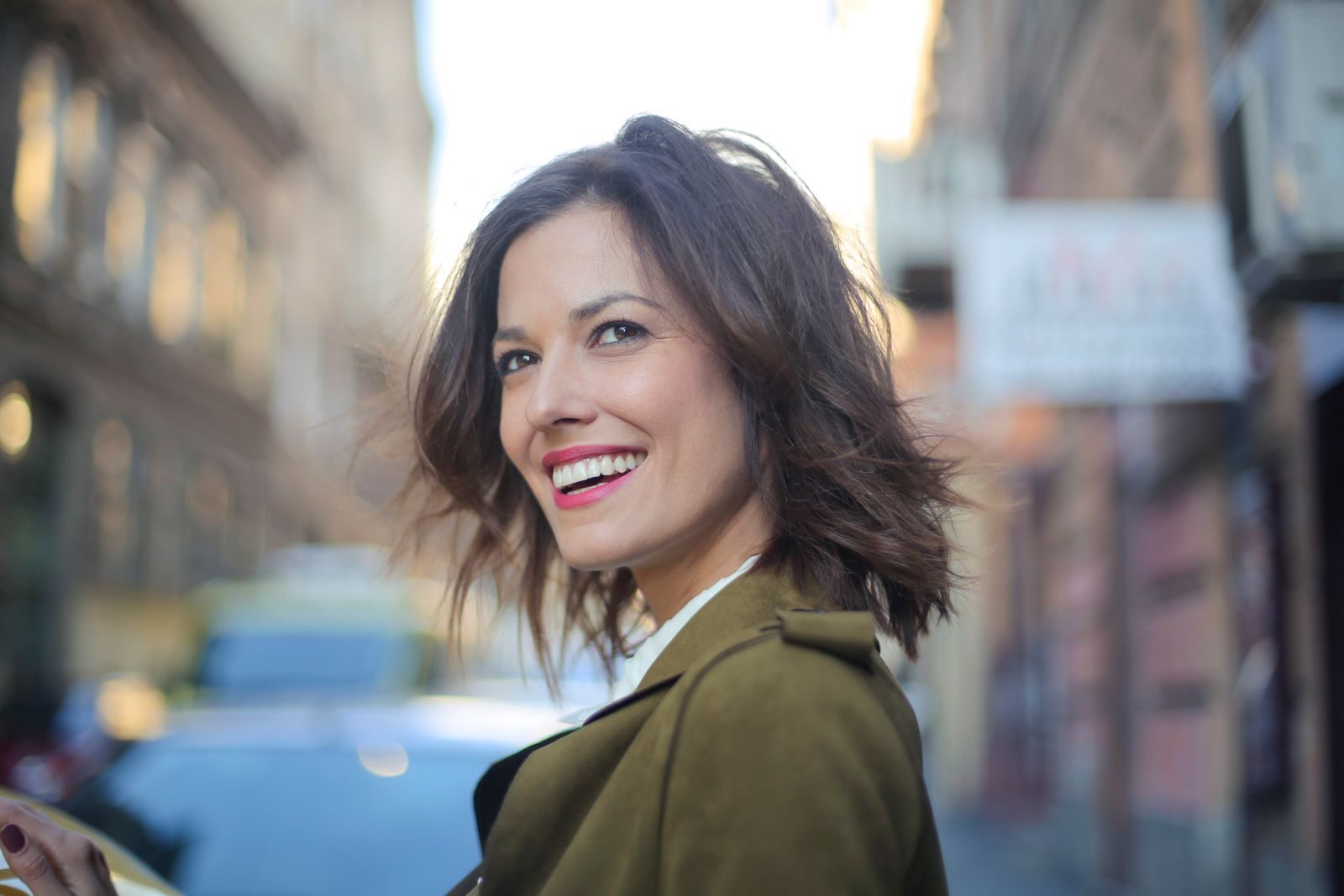 Revolutionizing Facial Rejuvenation: The Role of Injectables in Modern Aesthetics Portrait of a smiling woman standing on a city street in a green coat, looking away delightfully.