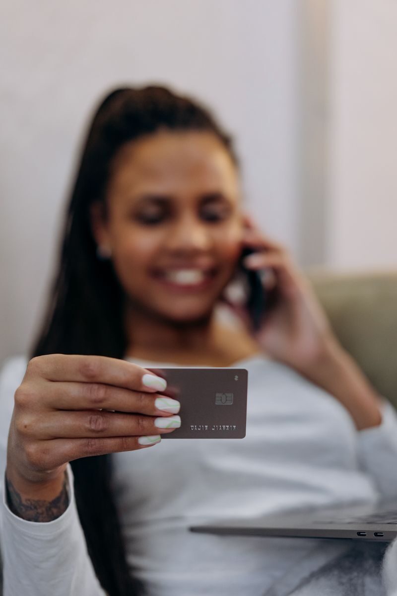 5 Steps to Get Over Your Fear of Credit Focused shot of a woman holding a credit card, engaging in a phone conversation, depicting online shopping or banking.