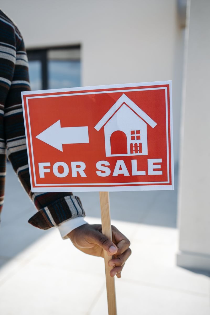 The Fast-Track Guide to Selling a House in Hillsboro Close-up of a hand holding a 'For Sale' real estate sign with a house icon outdoors.