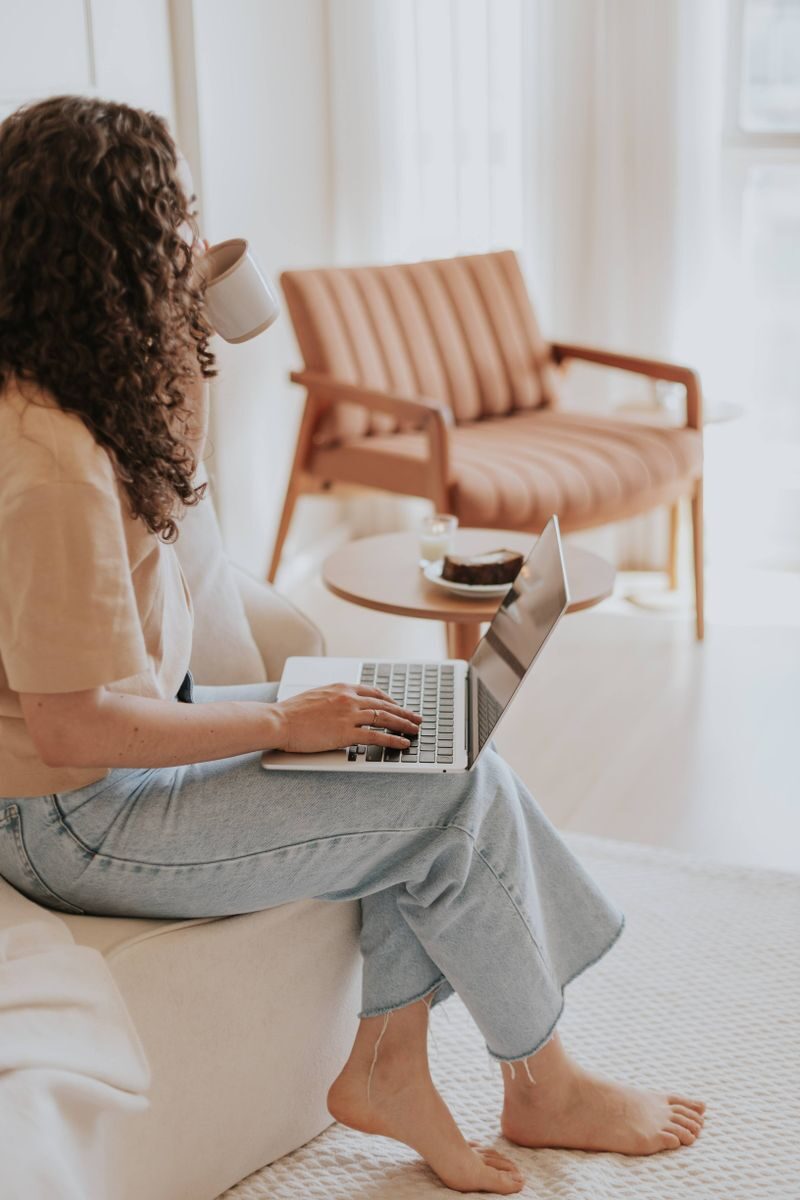 The Calm Home Checklist: Small Repairs That Quiet a Room Woman enjoying coffee while working on a laptop in a warm, minimalist living room setting.