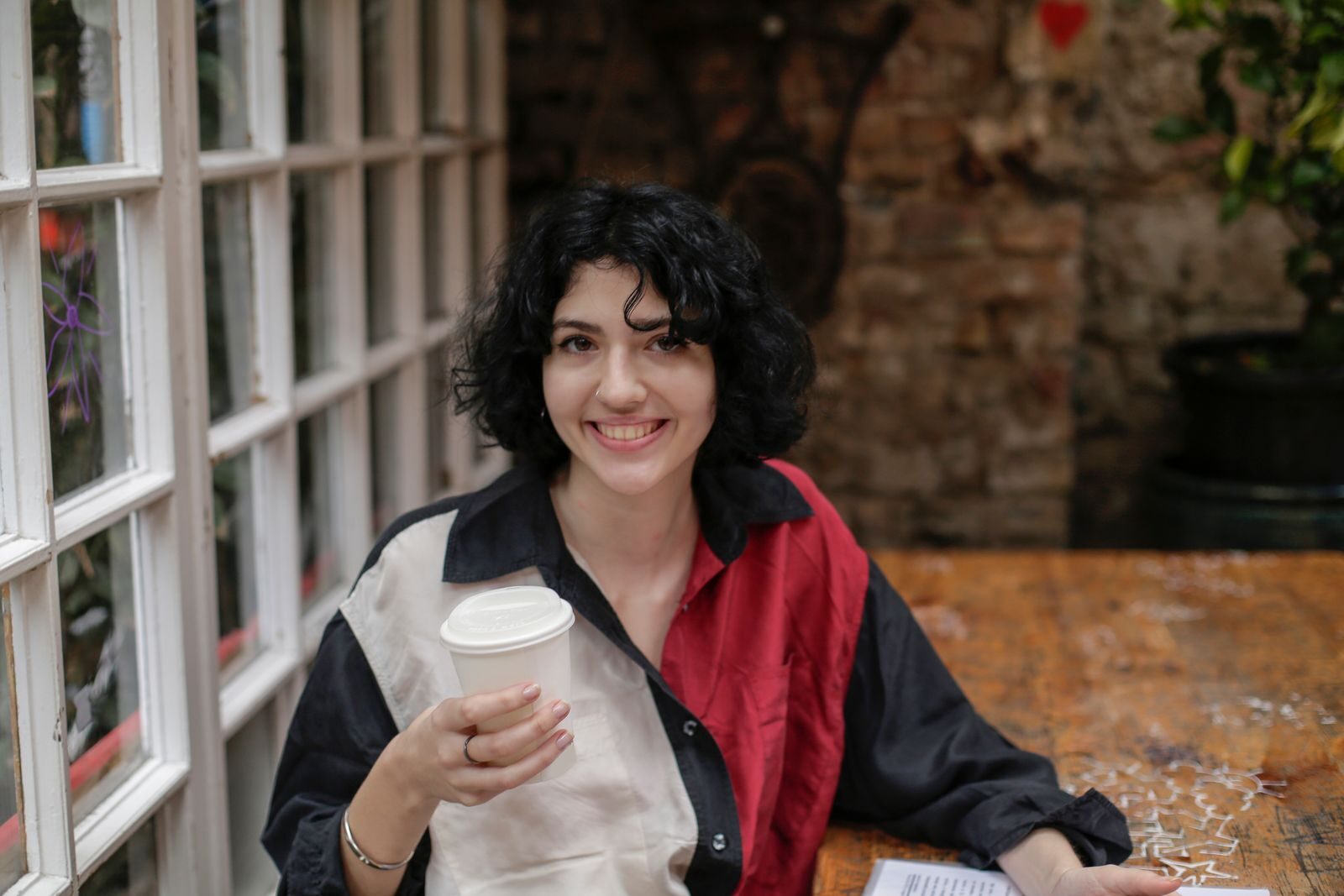 Death Cleaning Decluttering A cheerful woman with short hair enjoys coffee indoors, sitting at a cozy wooden table.