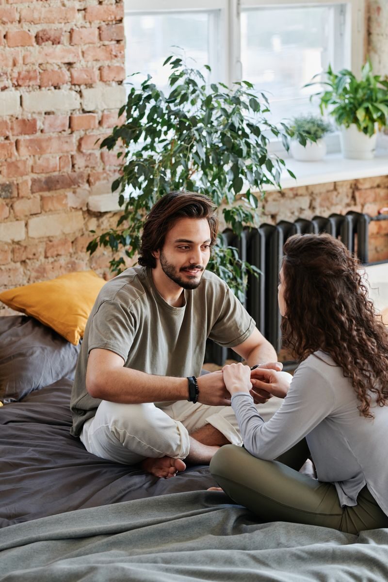 Addiction-Based Bond: Build Sober Stability With Couples Rehab California A couple sits together indoors, holding hands in a cozy home environment with a brick wall backdrop.