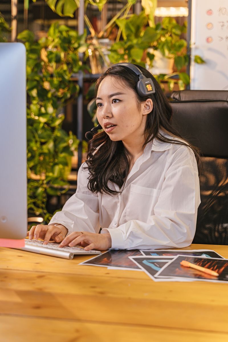 How Virtual Assistants Can Help Your Business Grow Asian woman using computer headset at office desk, focusing on work.