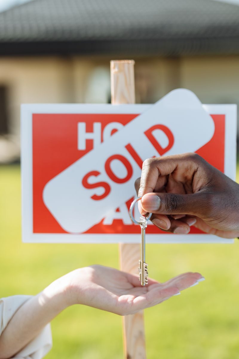 Selling a Home Quickly in Greenville, NC: A Checklist for Speed, Cost, and Certainty Key exchange in front of a sold sign, symbolizing successful real estate transaction.
