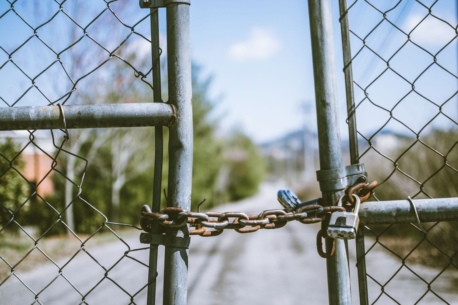 You Left Prison but the Sentence May Not Be Finished With You Close-up of a locked chain link fence with rusty chains and padlock, outdoors, in bright daylight.