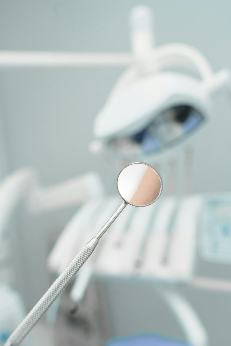 Can a Dental Savings Plan Help You Afford Regular Dental Visits? A dental mirror held in the foreground with a blurred dental chair behind