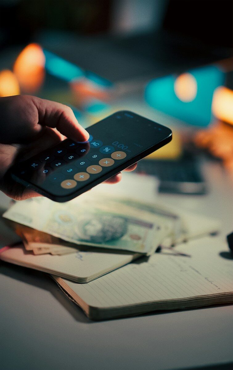 Building A Flexible Retirement Savings Plan Around Income, Debt, And Life Goals Hand using calculator on smartphone over money