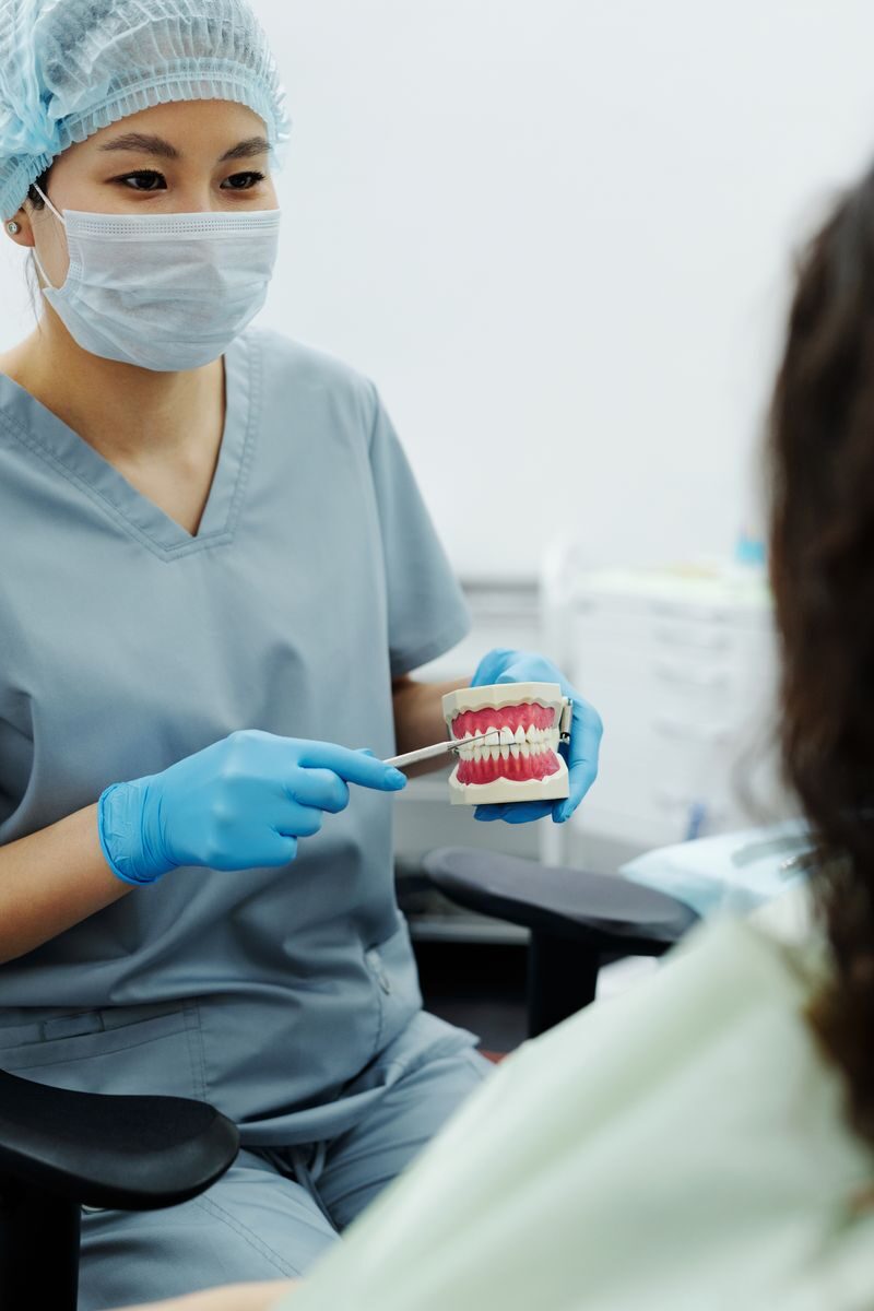 Dentures and the Emotional Side of Restoring a Complete Smile Female dentist in scrubs demonstrates teeth cleaning using a dental model to patient.